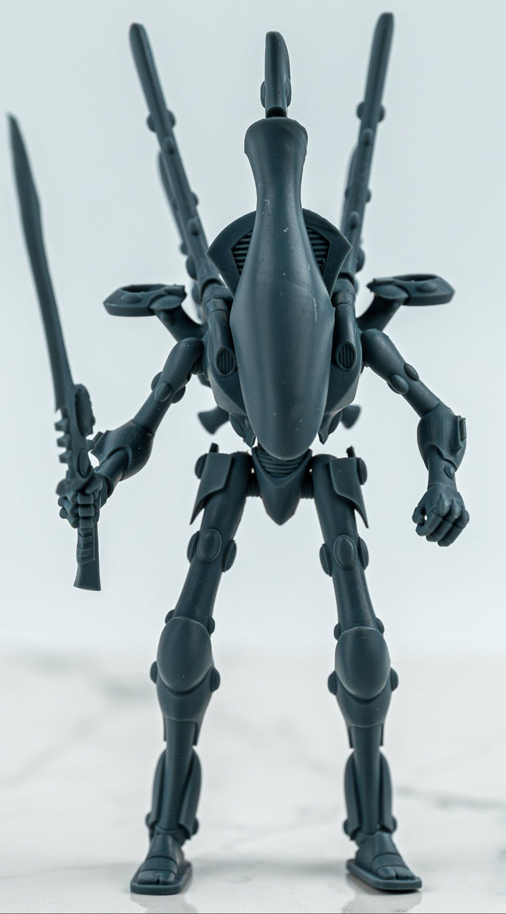 Grey sci-fi warrior model with elongated head armour, tall back-mounted details and a sword held upright.