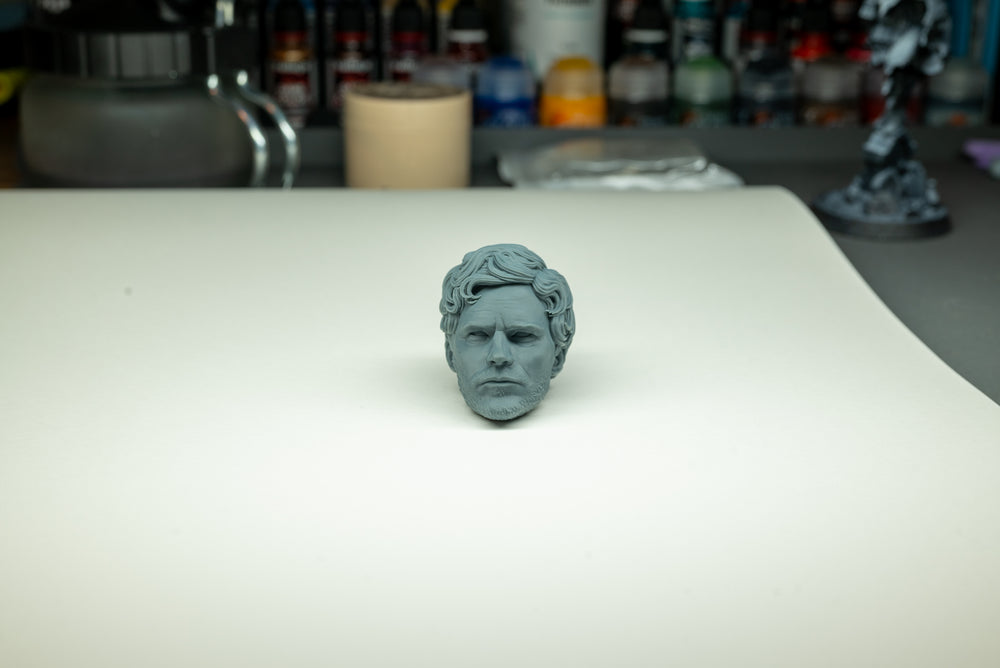 Grey unpainted character head with swept-back hair and detailed facial features on a studio work surface.
