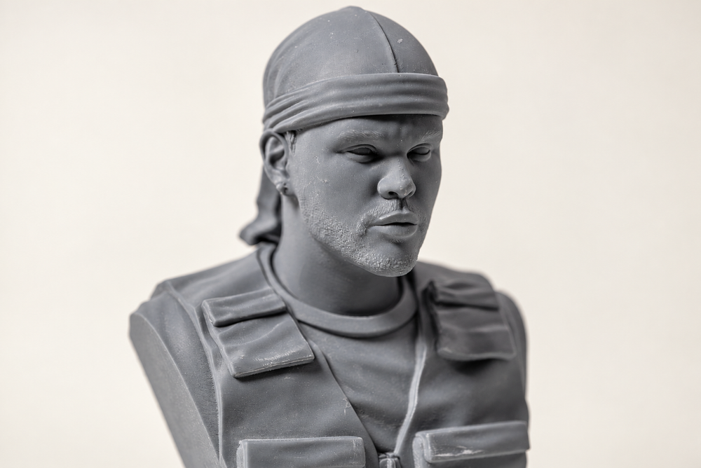 Grey portrait bust wearing a tied head covering and a detailed vest, photographed against a light background.